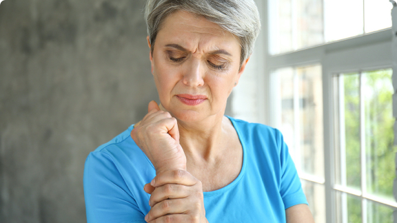 Elderly woman grasping wrist with discomfort.